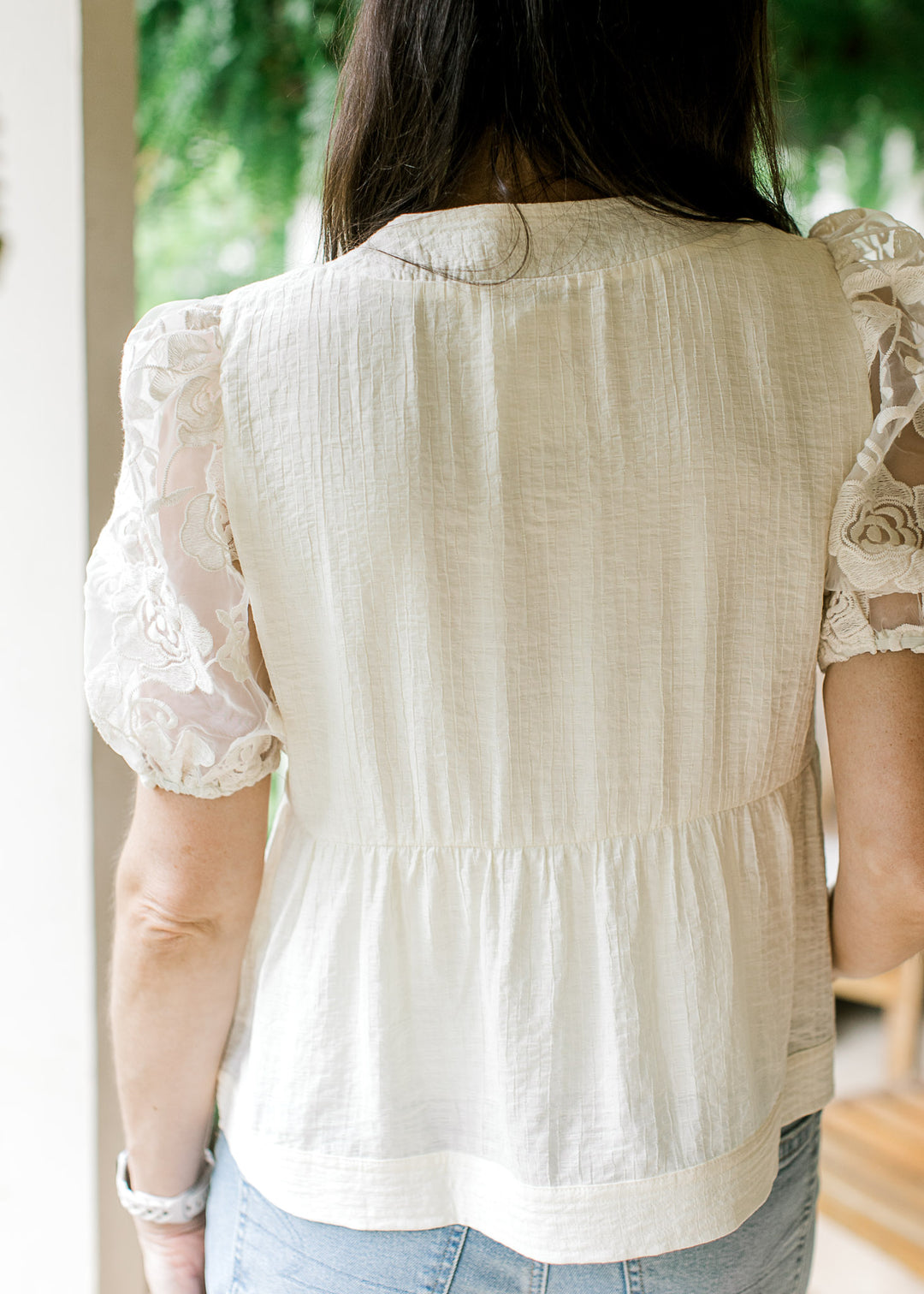 Back view of Model wearing a cream top with subtle textured bodice and sheer floral short sleeves.