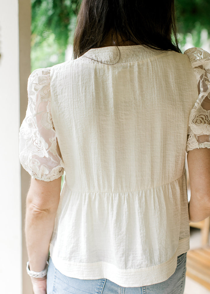 Back view of Model wearing a cream top with subtle textured bodice and sheer floral short sleeves.