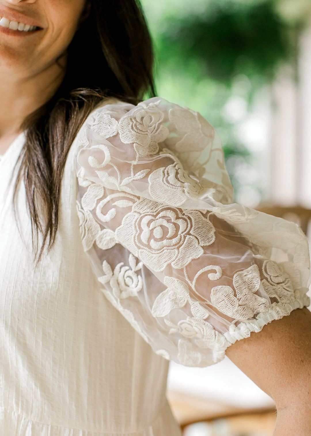 Close up of sheer floral bubble short sleeves on a cream babydoll top with subtle texturing.