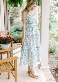 Model wearing a sleeveless white midi with green and blue floral, square neck, and lace scalloping. 