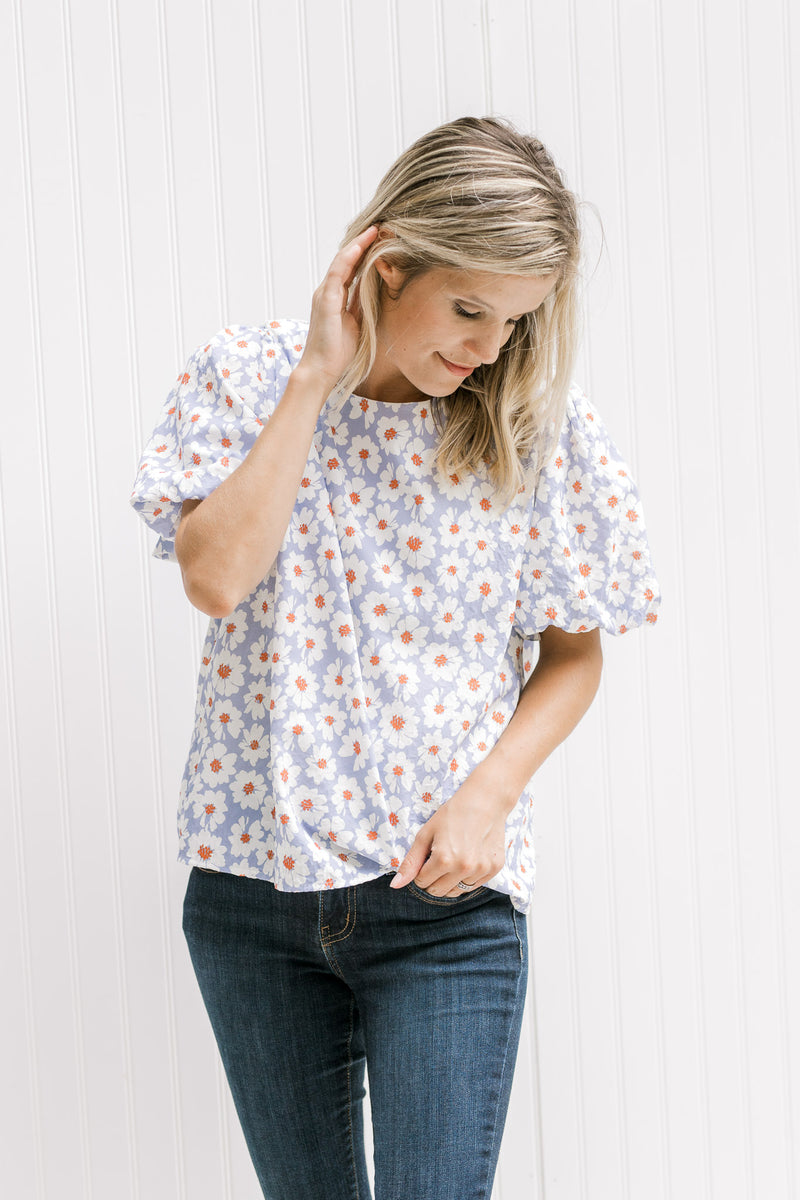 Model wearing a lavender top with a cream daisy pattern, crinkle material and short puff sleeves. 