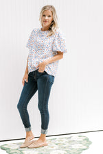 Model wearing jeans with a lavender top with a cream daisy pattern and short puff sleeves. 