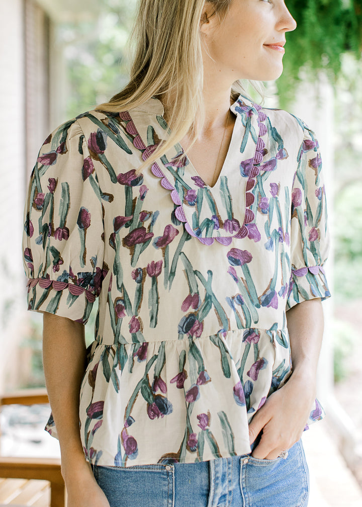 Model wearing a beige short sleeve babydoll top with lavender and blue floral. 