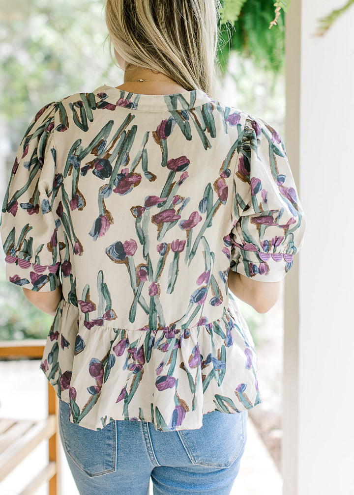 Back view of Model wearing a beige short sleeve babydoll top with lavender and blue floral. 