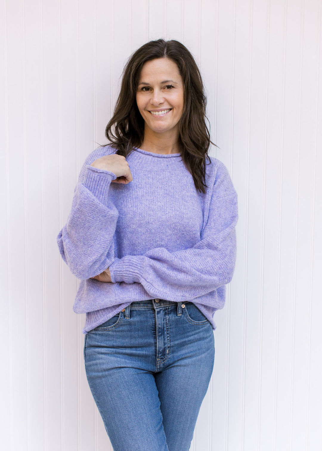 Model wearing jeans with a lavender knit sweater with long sleeves, rolled hems and a round neck. 