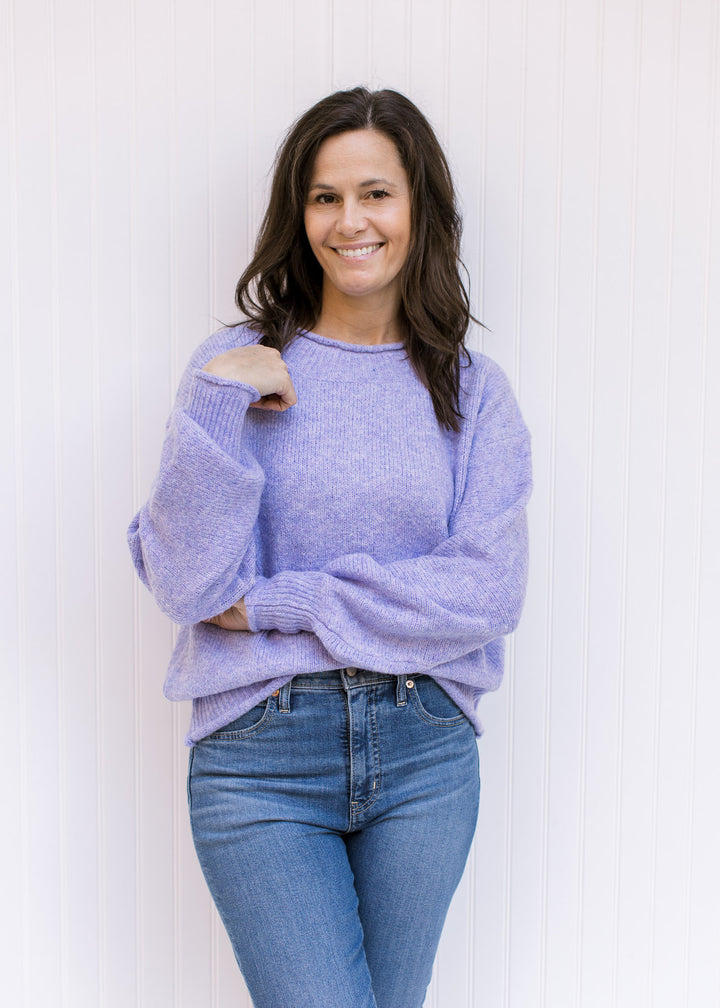 Model wearing jeans with a lavender knit sweater with long sleeves, rolled hems and a round neck. 