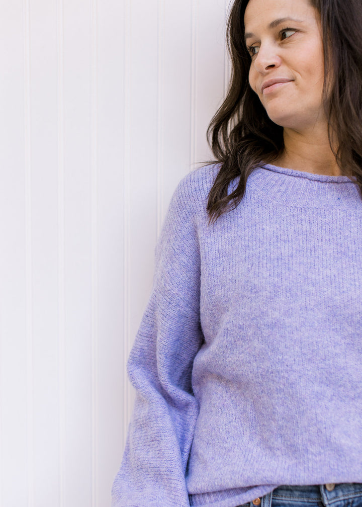 Close up of rolled hem on a round neck of a lavender kit sweater with long sleeves. 