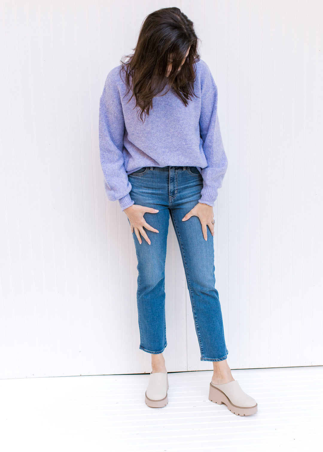 Model wearing jeans and mules with a long sleeve lavender sweater with rolled hems and a round neck.