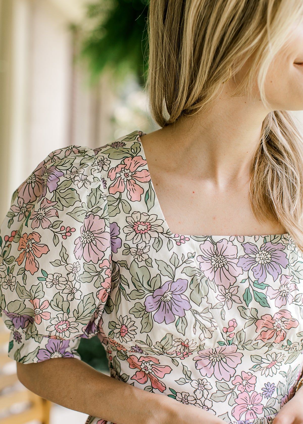 Close up of square neck and bubble short sleeve on cream dress with pink, purple and green floral.