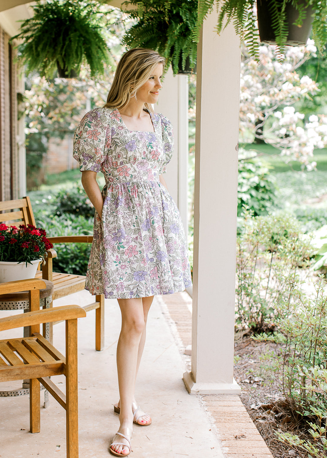 Model wearing sandals and a short sleeve, off white above the knee dress with colorful floral.
