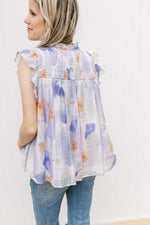 Back view of Model wearing a cream top with lavender and orange watercolor and flutter cap sleeves.