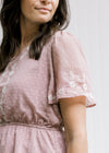 Close up of flutter short sleeves and elastic waistband on a lavender top with cream embroidery. 