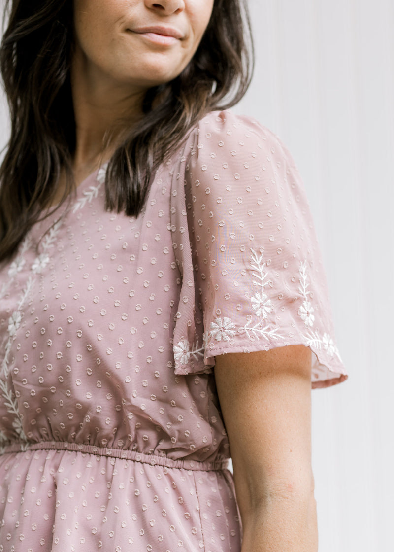 Close up of flutter short sleeves and elastic waistband on a lavender top with cream embroidery. 