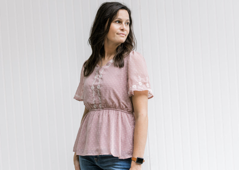 Model wearing a lavender short sleeve top with a cream embroidery and an elastic waistband. 