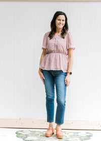 Model wearing jeans and sandals with a short sleeve lavender top with cream embroidered floral. 