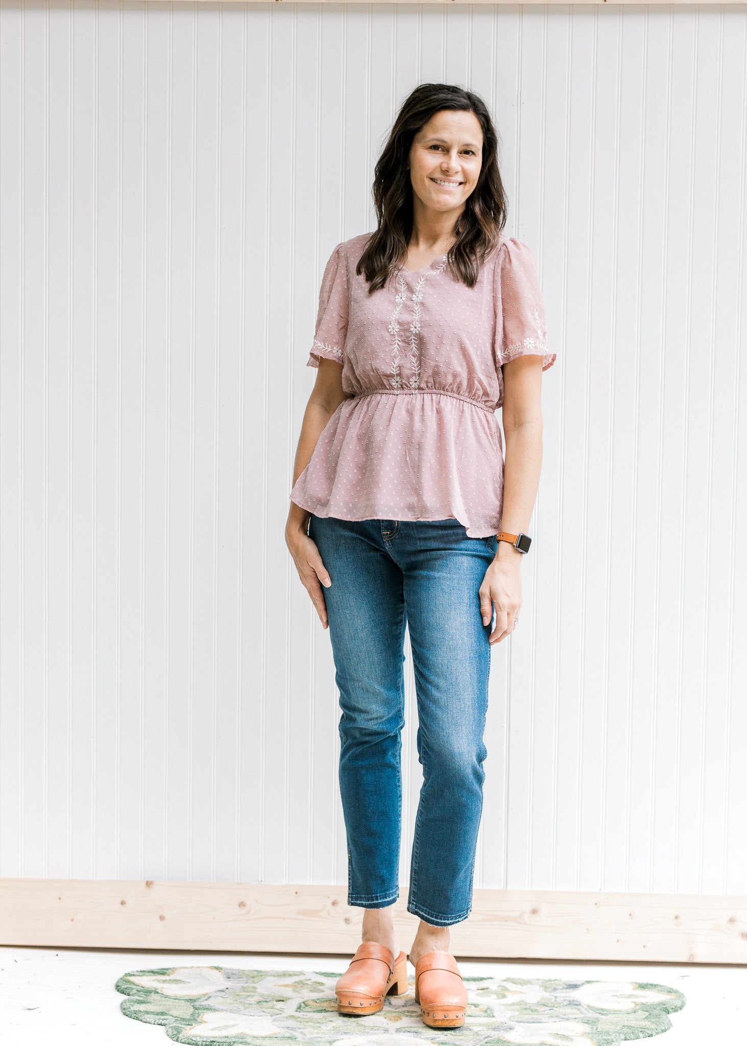 Model wearing jeans and sandals with a short sleeve lavender top with cream embroidered floral. 