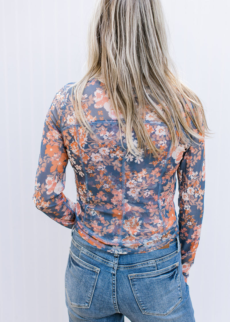 Back view of Model wearing a blue long sleeve top with rust and cream flowers and a round neck. 