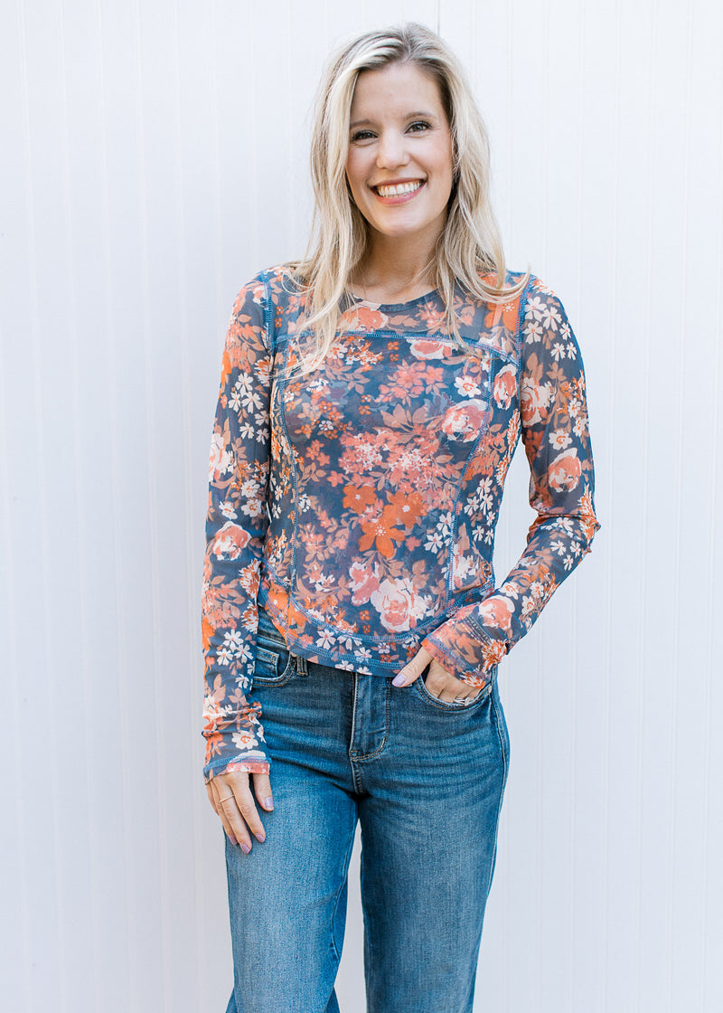 Model wearing a sheer blue top with rust and cream flowers, long sleeves and a round neck. 