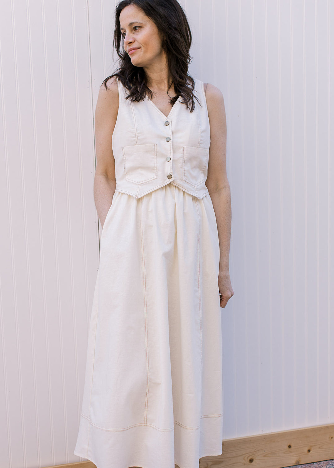 Model wearing a cream midi dress with a button-front v-neck vest and flowy attached skirt. 