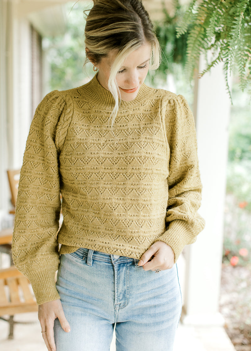 Model wearing a mustard knit sweater with pleated shoulders, long sleeves and a mock neck.