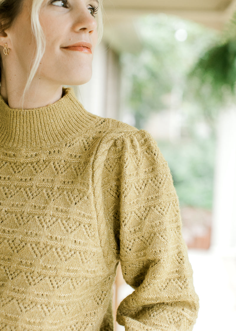 Close up on pleated shoulder and mock neck on a mustard colored long sleeve sweater. 