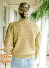 Back view of Model wearing a mustard sweater with pleated shoulders, long sleeves and a mock neck.