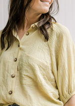 Close up of button closure and 3/4 bubble sleeves on a model in a lemon grass colored top. 