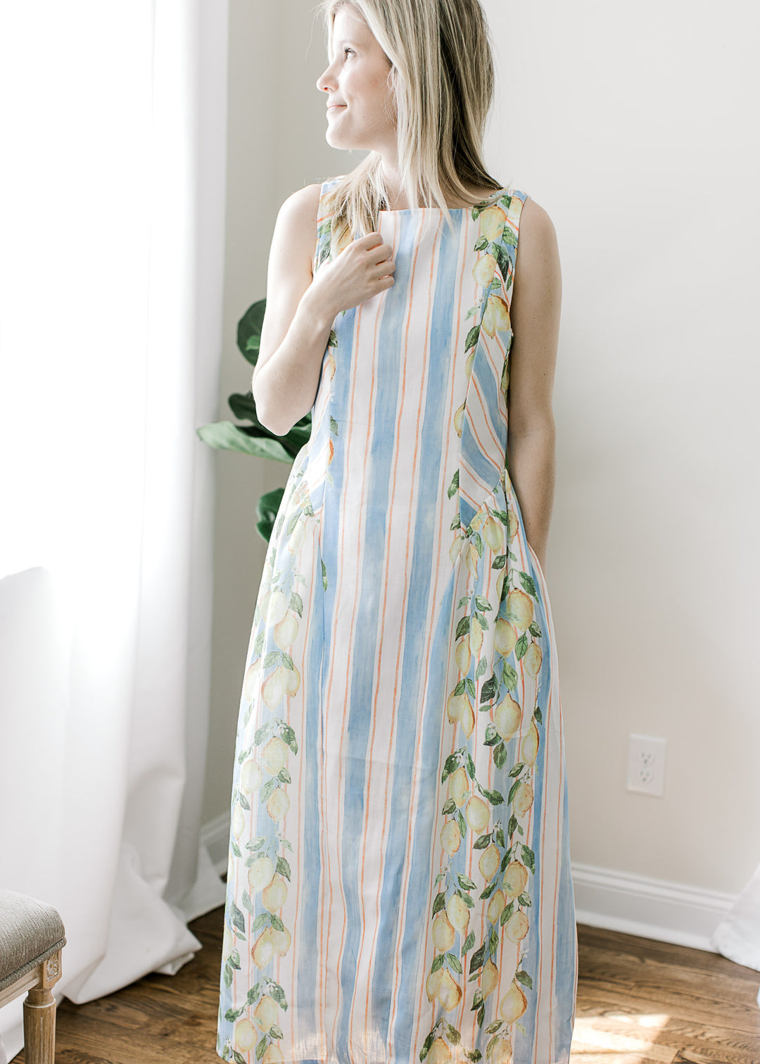 Model wearing a sleeveless white and blue striped midi with lemon detail on the outside edges. 