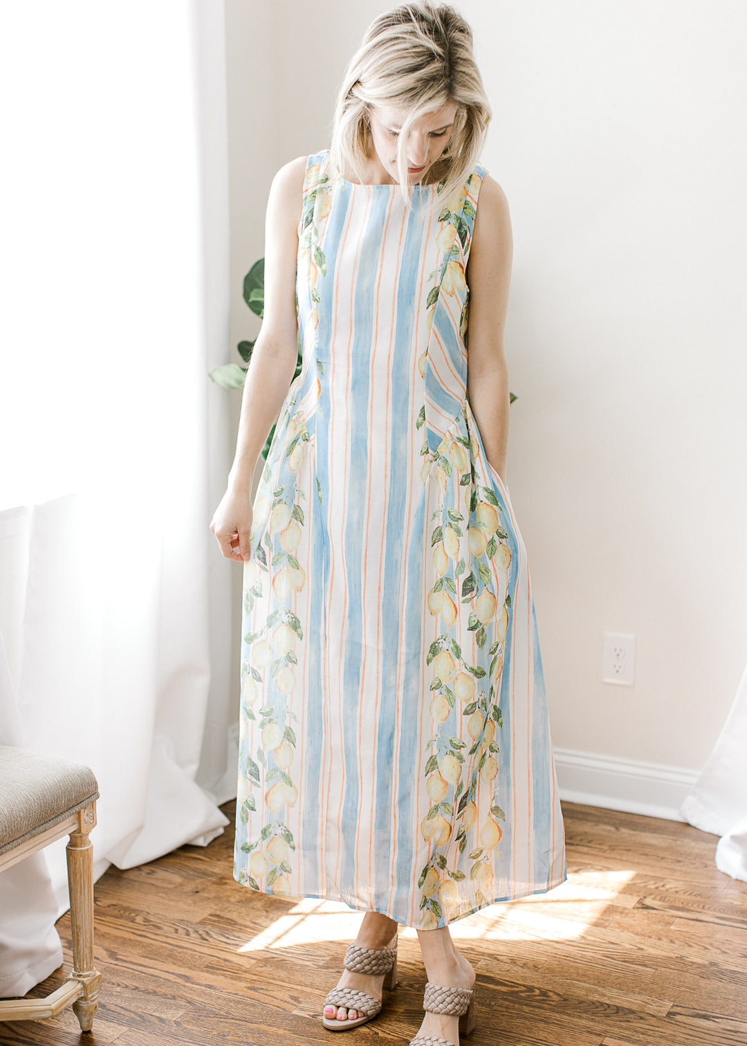 Model wearing a sleeveless white and blue striped midi with lemon detail, pockets and back zipper.