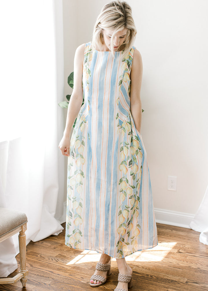 Model wearing a sleeveless white and blue striped midi with lemon detail, pockets and back zipper.