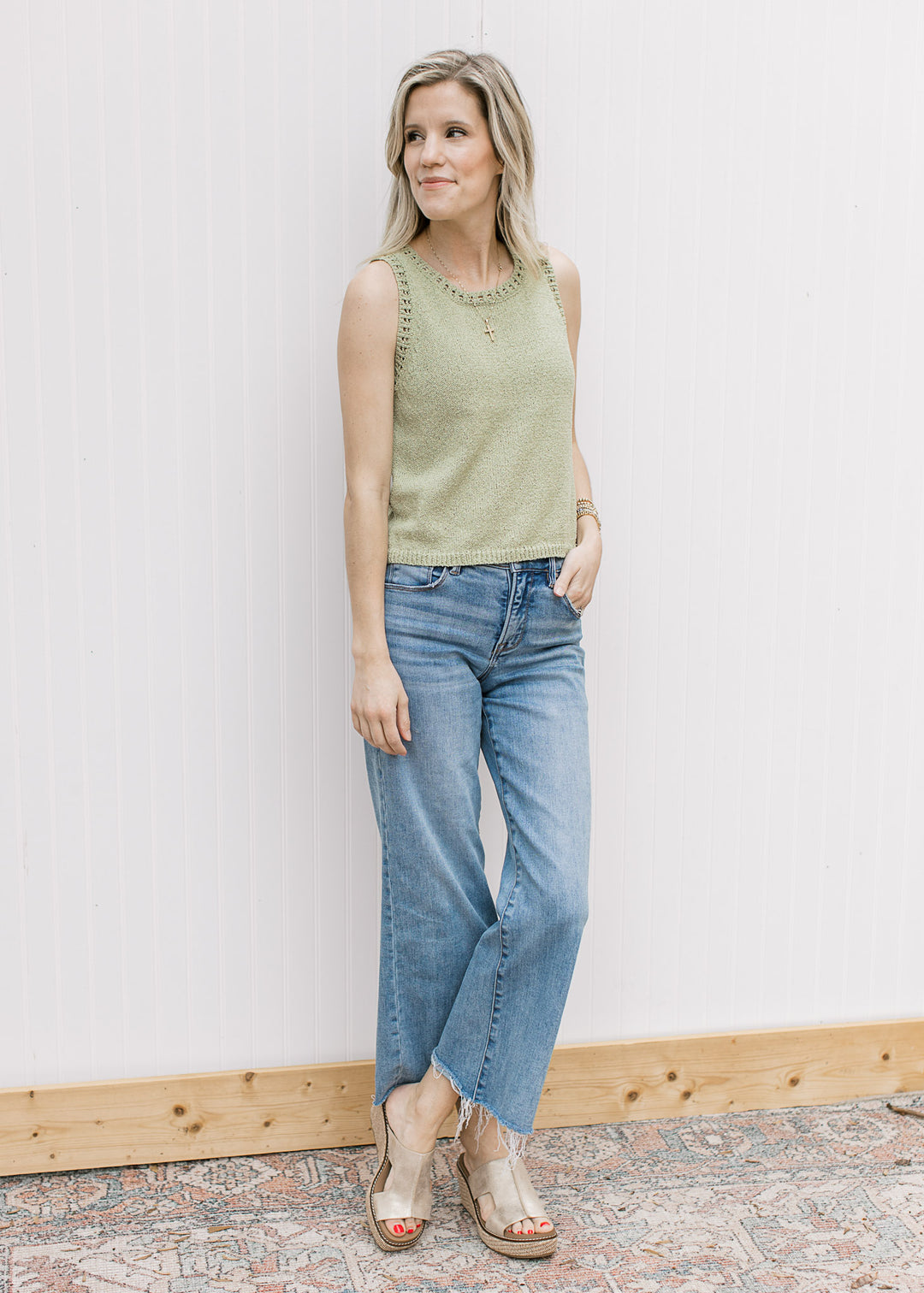 Model wearing a light green sleeveless sweater with a round neck and pen weave details. 