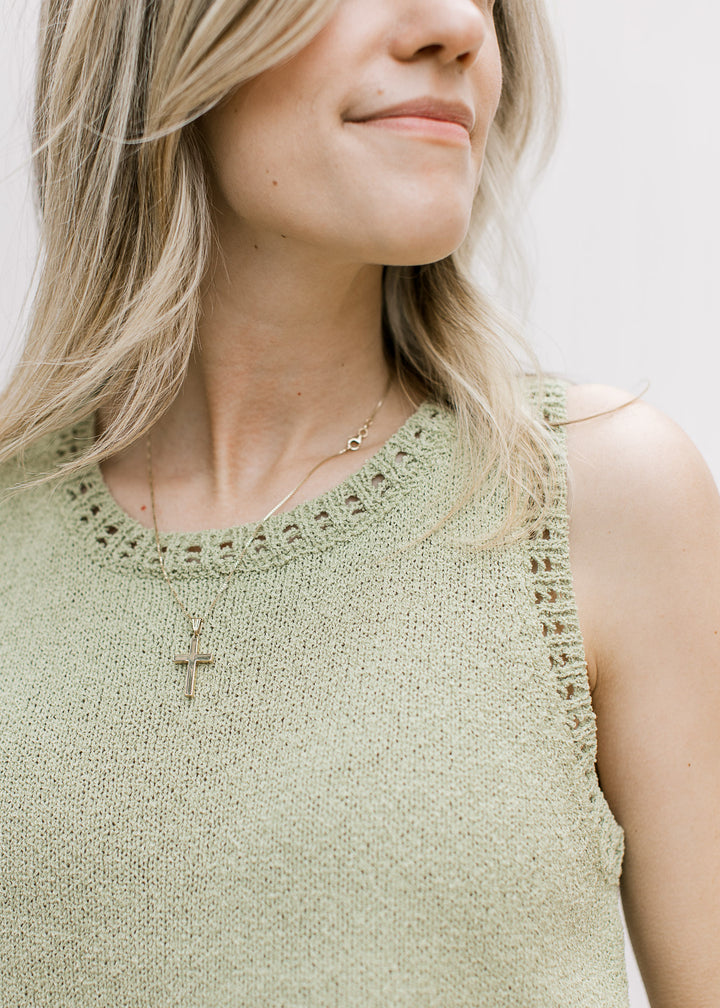 Close up of open weave at round neck and sleeves of a sleeveless light green sweater. 