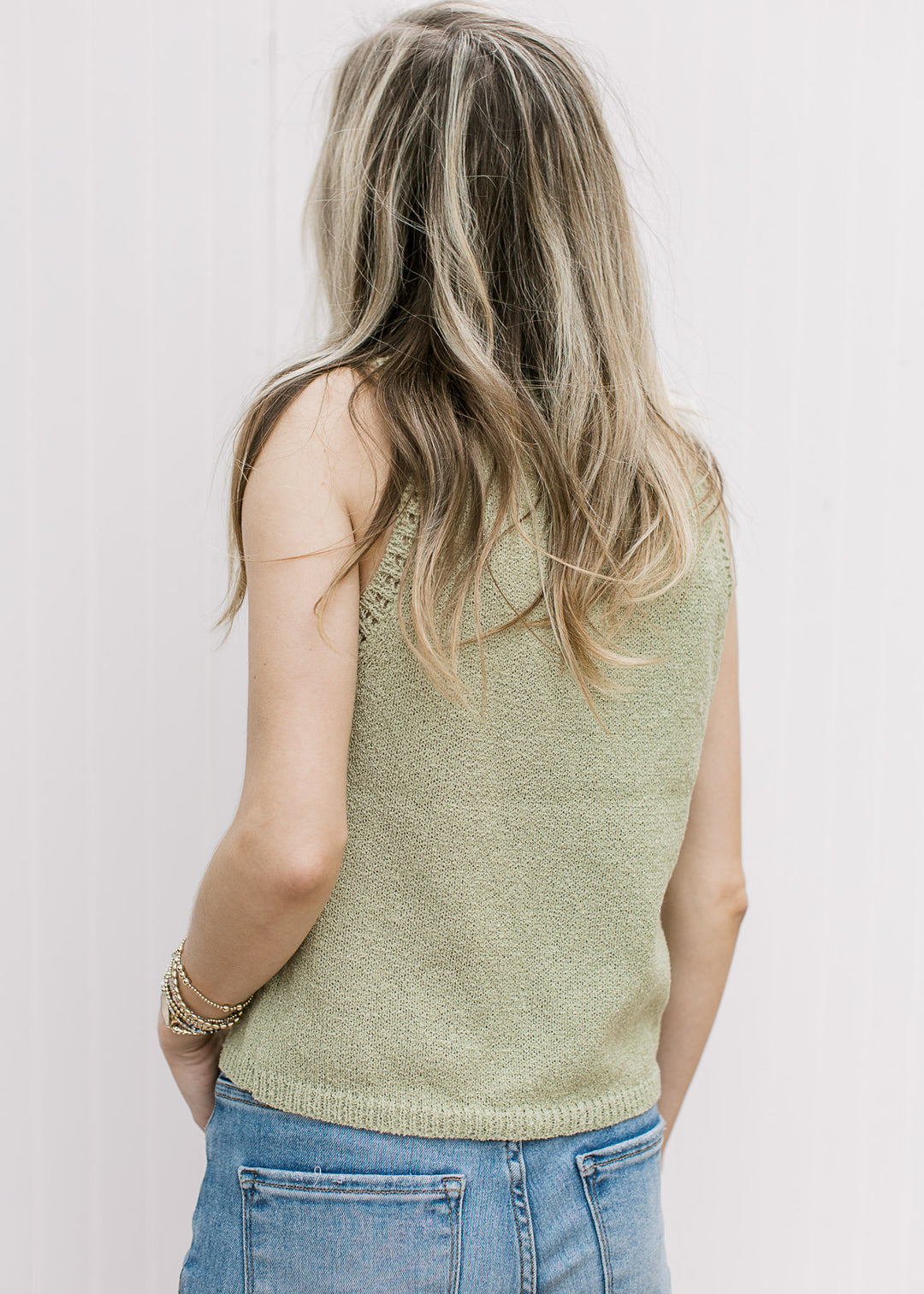 Back view of Model wearing a slightly cropped, light green sleeveless sweater with a round neck. 