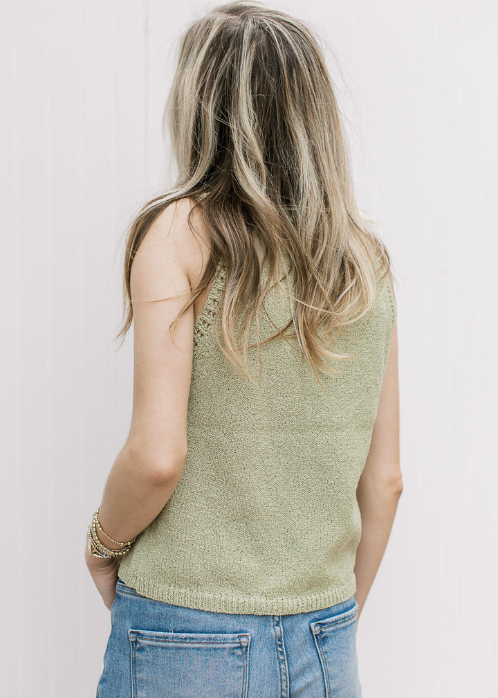 Back view of Model wearing a slightly cropped, light green sleeveless sweater with a round neck. 