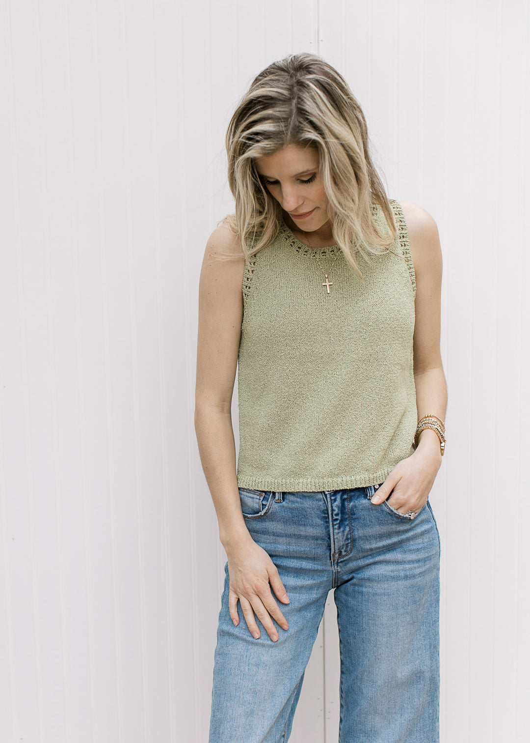 Model wearing jeans and a light green sleeveless sweater with an open weave details. 