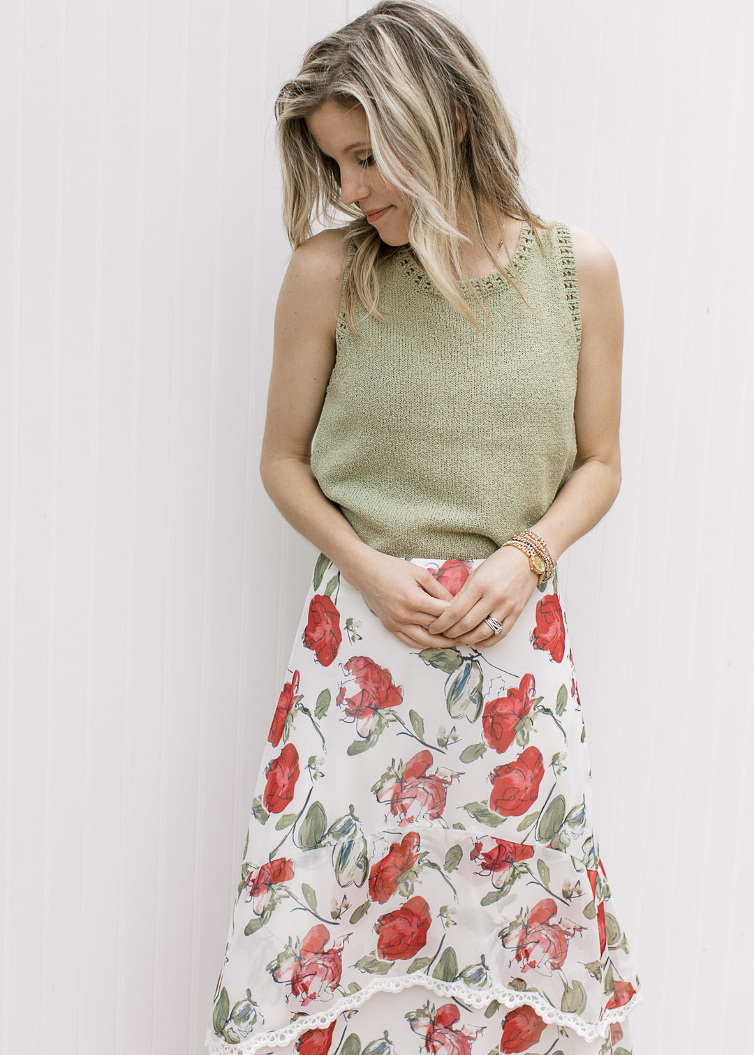 Model wearing a pale green sleeveless sweater with an ivory skirt with red floral. 