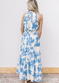 Back view of model wearing a white maxi with light blue floral, an elastic waist and racer back.