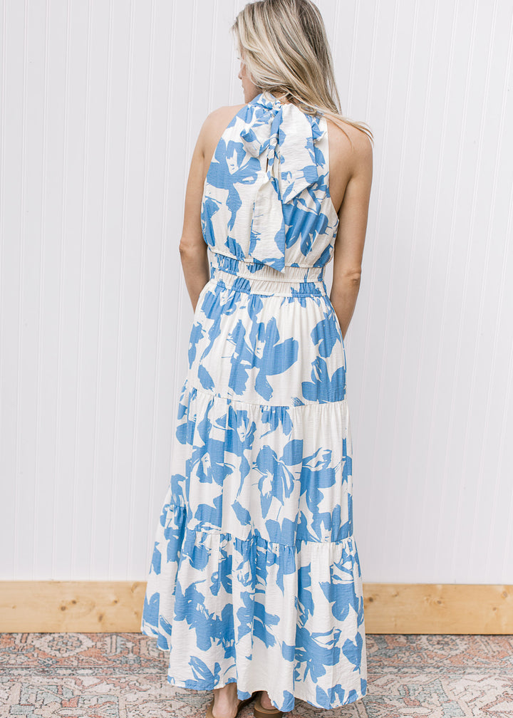 Back view of model wearing a white maxi with light blue floral, an elastic waist and racer back.