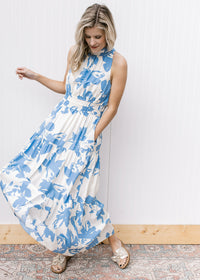 Model wearing a white maxi with light blue floral, an elastic waist, mock neck and racer back.