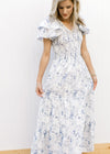 Model wearing a white maxi with blue floral, smocked bodice and double ruffle short sleeves.