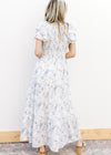 Back view of Model wearing a white maxi with blue floral, smocked bodice and ruffle short sleeves.