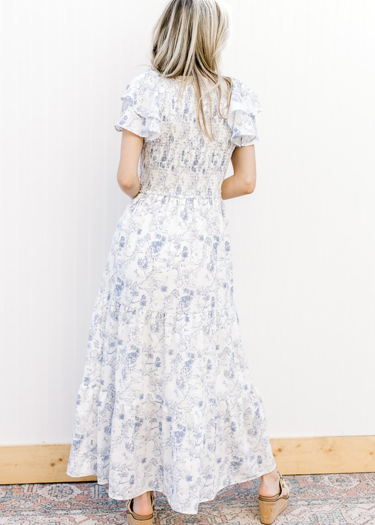 Back view of Model wearing a white maxi with blue floral, smocked bodice and ruffle short sleeves.