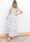 Model wearing sandals and a white maxi with blue floral, smocked bodice and short sleeves.