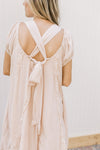 Back view of cross back detail with tie on a blush dress with a ruffle detail and short sleeves.
