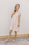 Model wearing sandals and a blush dress with a square neck, ruffle detail and short sleeves.