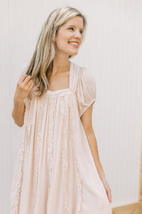Model wearing a blush dress with a square neck, ruffle detail and short sleeves. 
