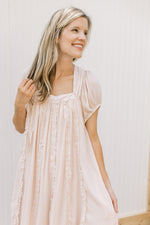 Model wearing a blush dress with a square neck, ruffle detail and short sleeves. 