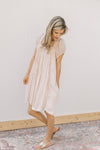 Model wearing a blush dress with a square neck, ruffle detail and pockets.