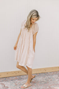 Model wearing a blush dress with a square neck, ruffle detail and pockets.