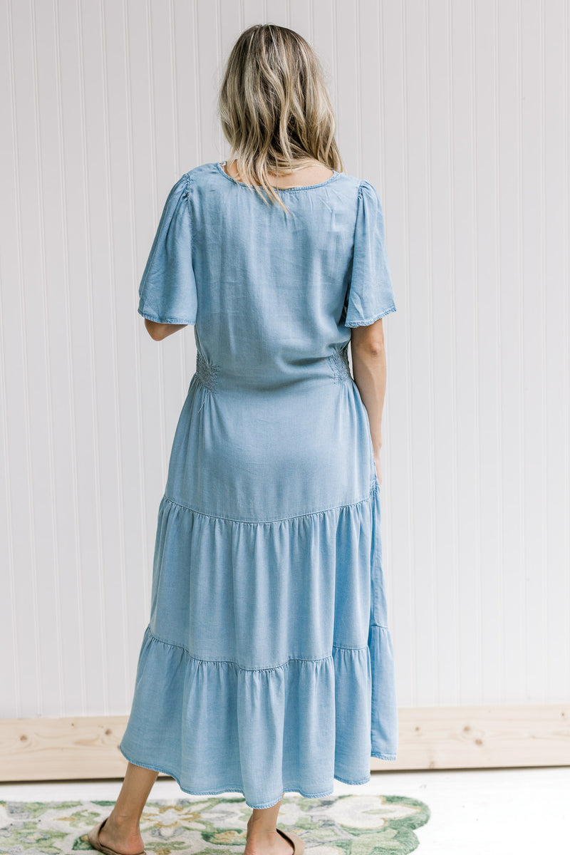 Back view of Model wearing a tiered midi with a light chambray color and short sleeves.